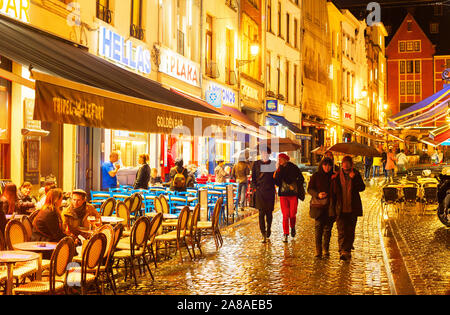 Brüssel, Belgien - 07 Oktober, 2019: Die Menschen gehen und sitzen in einem Restaurant in der Altstadt Einkaufsstraße von Brüssel im Regen in der Dämmerung Stockfoto