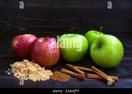 Granny Smith und Fuji Äpfel mit Zimtstangen, brauner Zucker, und Apple Pie Spice auf einem dunklen Hintergrund Stockfoto