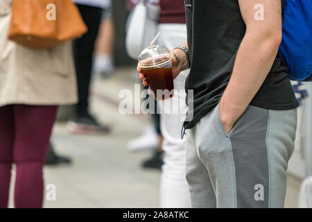 Junger Mann mit einem Plastik Tasse kalten Kaffee mit seiner Hand auf Pocket legere Kleidung, im Freien Stockfoto