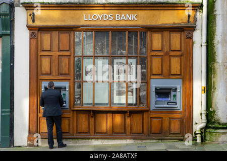 Ein Mann im Anzug mit einem Geldautomaten oder ATM außerhalb einer alten Lloyds Bank Stockfoto