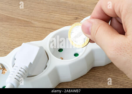 Frau Hand eine Münze über die Stromversorgung Verlängerungskabel outlet über braun Holz- Oberfläche. Kosten für Strom und teure Energie Konzepte. Close-up. Stockfoto