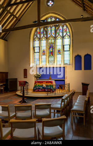 Der Altar der Anglikanischen Kirche mit einem Glasfenster hinter von Stühlen umgeben Stockfoto
