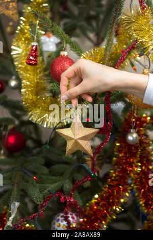 Frau Kleider ein Weihnachtsbaum für Weihnachten. Die Hand der Frau hält einen goldenen Stern und hängt ein Weihnachtsbaum Verzierung. Stockfoto