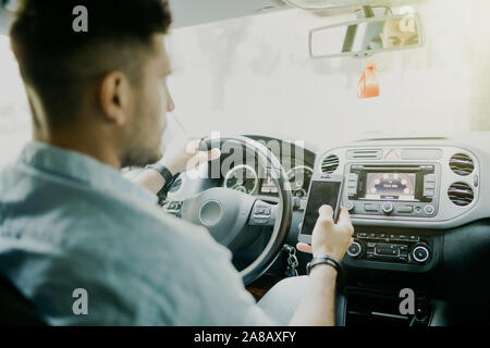 Immer in Kontakt. Obere hintere Ansicht des jungen Mannes in formale über sein Smartphone während im Auto sitzen Stockfoto