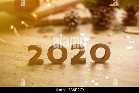 2020 Neue Jahr Holz Anzahl mit funkelnden festliche Weihnachtsbeleuchtung bokeh und Geschenke mit Tannenzapfen. Holz Hintergrund. Stockfoto