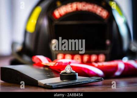 Eine Teardrop, oder Birne, geformte Diamond Engagement Ring oben auf einer Hochzeit Band und Fireman ax mit einem feuerwehrhelm Unscharf im Hintergrund. Stockfoto