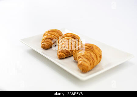 Seitenansicht von drei köstliche, frisch gebackene Croissants und auf einem weißen Teller auf weißem Hintergrund Stockfoto