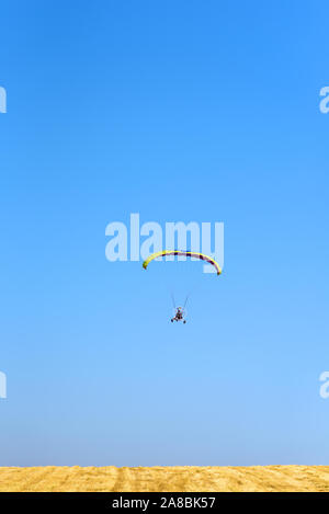 Powered Gleitschirm Fallschirm gegen den blauen Himmel und das gelbe Feld. Motorschirm fliegen in sonniger Tag. Freiheit und Sommerurlaub Konzept, extreme Sport. Stockfoto