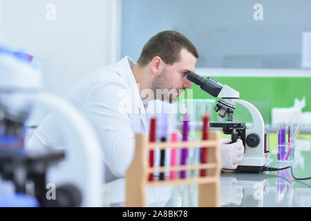 Junge männliche Wissenschaftler durch ein Mikroskop im Labor Forschung suchen, mikrobiologische Analyse, Medizin. Stockfoto