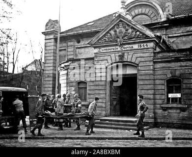 Ein Fahrzeug mit der hinteren Türen geöffnet sitzt vor einem Gebäude aus dem 19. Jahrhundert, in ein Lazarett umgewandelt wurde. (Unter dem Giebel ist eingraviert: "Turnverein Borna 1844.') Zwei Soldaten tragen eine verletzte Soldaten auf einer Bahre aus dem Fahrzeug auf die offene Tür eines Gebäudes. Stockfoto