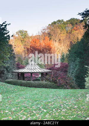 Brilliant autumn colors as background to garden pavilion / gazebo, green trees and large green lawn. Vertical format. No people. Copy space. Stockfoto