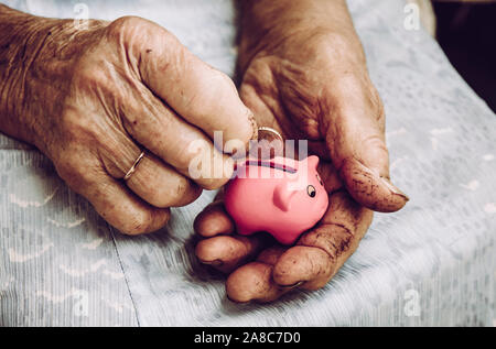Nahaufnahme der alten schmutzigen, rauen älteren älteren, pensionierten Frauen, die die winzige pinkfarbene Schweinebank halten. Kleines Rentenkonzept. Stockfoto