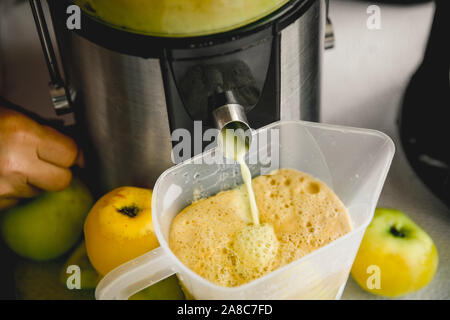 Frischen apfelsaft zu Hause im Herbst zumachen. Frischer Saft fließt durch die Maschinenröhre in eine Kanne. Stockfoto