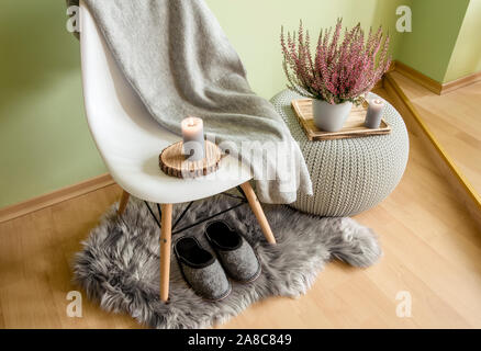 Kunststoffstuhl mit Holzbeinen mit grauer Wollpflaster, gestricktem Kunststofftisch, gefälschter Schaffelldecke mit Filzschuhen und Heidekraut in Blume Stockfoto