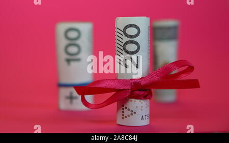 Rolle gerollt 200 Polnische Zloty mit roter Schleife gebunden, hinter zwei Rollen von 100 Zloty in Soft Focus, Nahaufnahme, Konzept der wirtschaftlichen/finanziellen Geschenk. Stockfoto