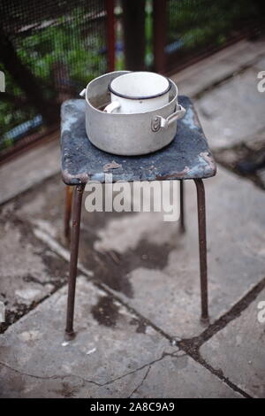 Altes Geschirr auf retro Hocker. Aluminium Schwenk und emaillierten Becher auf einem Stuhl. Ländlichen Hof. Stockfoto