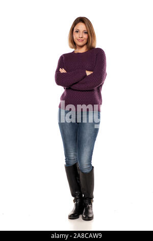 Junge lächelnde Frau in einem lila Pullover und Jeans mit verschränkten Armen Stockfoto