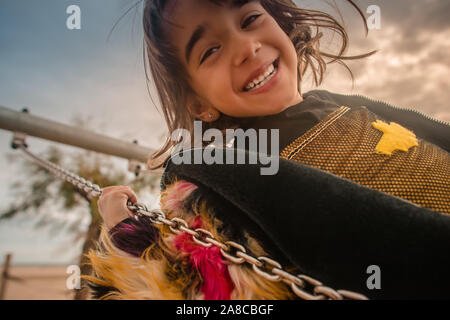 Nahaufnahme von einem jungen europäischen Mädchen glücklich spielen auf einer Schaukel an einer im Park tragen eine Fledermaus Kostüm. Stockfoto