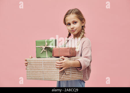 Portrait von kleinen Mädchen mit blondem Haar Holding verpackte Geschenksets ihr zu ihrem Geburtstag und Kamera über rosa Hintergrund Stockfoto