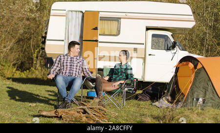 Hipster Freund küsst seine Freundin Hand beim Sitzen auf Camping sitzen vor ihren vintage Camper. Entspannende Woche-end Stockfoto