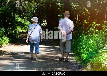 Paar mittleren Alters ist zu Fuß in den Wald. Holz auf den Seiten von Trail. Ältere Paare ist Walking im Green Park auf Urlaub. Sommertag. Stockfoto