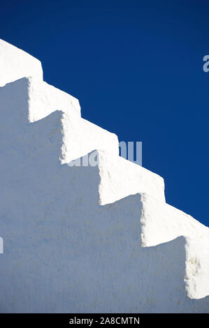 Detail des gestuften weißen Stuck-Dachs, das in den lebhaften blauen mediterranen Himmel in Mykonos, Griechenland führt Stockfoto