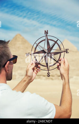 Touristen, die einen altmodischen Kompass halten, stiegen in heller Sonne vor den Großen Pyramiden Ägyptens auf Stockfoto