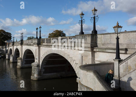 Vom Südufer der Themse ist die Architektur der Kingston Bridge, wo ein Fußgänger hält einen selfie Foto aufzunehmen, am 7. November 2019 in Kingston, London, England gesehen. Eine Kreuzung hat am Kingston existiert seit der Antike und dieser Version von Kingston Bridge von Herbert für £ 26.800 konstruiert wurde und durch die Herzogin von Clarence (die zukünftige Königin Adelaide) am 17. Juli 1828 eröffnet. Von Portland aus Stein gebaut, es besteht aus fünf elliptische Bögen. Stockfoto