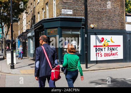 Ein paar Spaziergang, vorbei an Boutiquen und ein Wandbild mit der Meldung keine Panik Es ist organisches in Islington, London, England, UK. Stockfoto