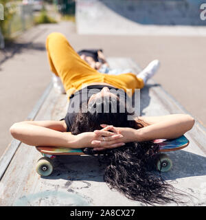 Junge Frau liegend auf Skateboard in urbanen Skate Park Stockfoto