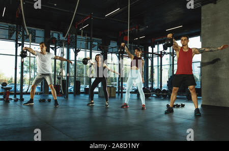 Eine Gruppe von muskulöse Athleten, trainieren Sie im Fitnessraum. Gymnastik, Training, Fitness Workout Flexibilität. Aktiven und gesunden Lebensstil, Jugend, Bodybuilding. Training mit Gewichten, Kniebeugen. Stockfoto