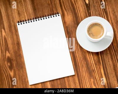 Kaffee in weiße Tasse, und öffnen Sie den Editor mit einem sauberen weißen Seite auf braunem Holz- Tabelle, Ansicht von oben, diagonal Stockfoto
