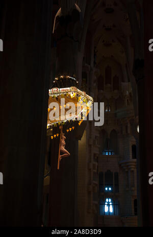 Sagrada Familia - Interieur. Hängende Skulptur Kronleuchter Jesu unter hohen Säulen vor dem Hintergrund der Glasfenster in warmen Farben. Stockfoto