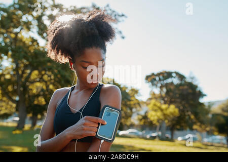 Aktive sportliche junge afrikanische amerikanische Frau, Musik smart phone vor Fitness im Freien Training im Park an einem sonnigen Tag Stockfoto