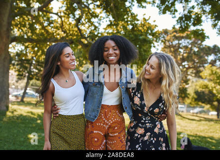 Porträt einer Gruppe von glücklich drei verschiedene junge Frauen lachen und Spaß in den Park an einem sonnigen Tag umarmen beim Gehen Stockfoto
