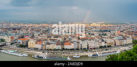 Antenne Panorama der Stadt Budapest und die Donau, Kreuzfahrtschiffe und einen bunten Regenbogen in den Himmel über der Stadt. Blick vom Gellertberg. Stockfoto