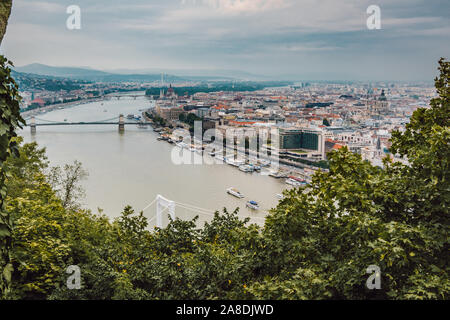 Ein schönes Panorama auf die Stadt Budapest und die Donau, die von den Zweigen und Blättern der Bäume umgeben. Blick vom Gellertberg. Stockfoto