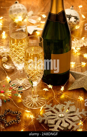 Champagnergläser und Flasche mit Weihnachtsbeleuchtung, Kugeln und silberne Sterne Dekorationen, auf einem Holztisch Stockfoto