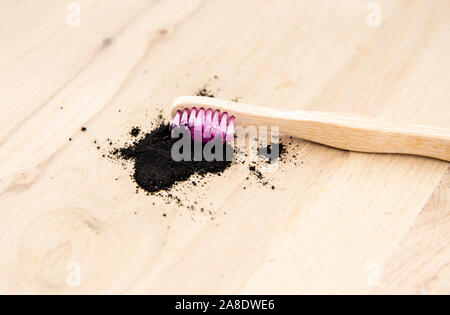 Rohstoff Aktivkohle Pulver auf hölzernen Hintergrund natürlicher Bambus Zahnbürste hinein. Holzkohle Zahnpasta Konzept. Minimalistische Komposition mit viel o Stockfoto