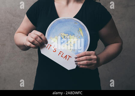 Flache Earther Konzept. Person, die glaubt, dass die Erde flach ist. Anonyme Frau mit flachen Erde Modell vor der Körper mit Text: Es ist flach. Iso Stockfoto