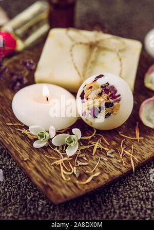 Verschiedene Whirlpool Produkte auf braunem Holz- fach cremige Badebombe, natürliche Seife mit Baumwolle string, getrocknete Blütenblätter, Wellness Kerzen, wesentliche Stockfoto