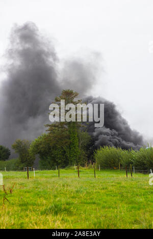 21. August 2019 einen dicken schwarzen Rauch von brennenden Gummireifen in unverantwortlicher Weise Füllen der Himmel auf einer Farm im County Fermanagh in Nordirland Stockfoto