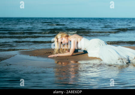 Porträt der jungen blonden Braut liegt auf Sand unter das Wasser, mit Blick auf die Kamera Stockfoto