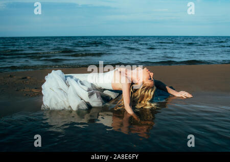 Porträt der jungen blonden Braut liegt auf Sand unter den Wasser, Suchen nach Stockfoto