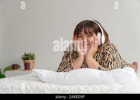 Übergewichtige Frau auf dem Bett liegend und Kopfhörer zum Hören von Musik. Das Konzept der komfortable Tag und Rest. Stockfoto