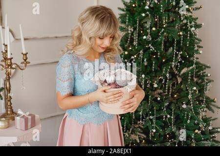 Junge Frau schmückt Weihnachtsbaum mit Weihnachten Spielzeug. Klassische Einrichtung in Weiß und Gold Stockfoto