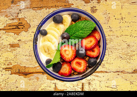 Schüssel mit Müsli und Obst, grüne Minze Blatt auf alten Holztisch. Nahaufnahme, Ansicht von oben, flach. Selektive konzentrieren. Stockfoto
