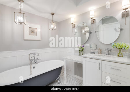 Eine schöne, weiße Badezimmer mit einem Stand alone clawfoot Badewanne mit Chrom Hardware. Blumen auf dem weißen Marmor Zähler nach oben. Stockfoto