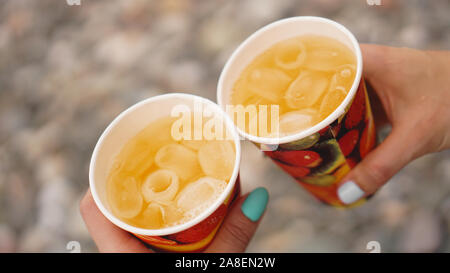 Männliche hand Pappbecher mit lemonaide auf dem Hintergrund der Steine, Kies Strand. Strand Ferienhäuser Konzept Stockfoto