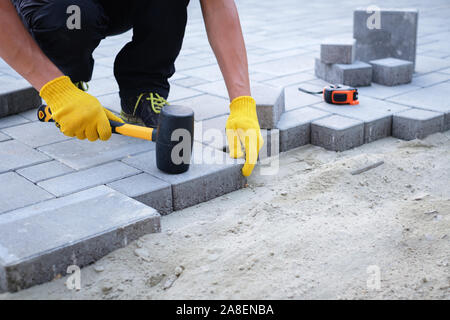 Der Master in gelb Handschuhe legt Pflastersteine in Schichten. Garten Stein weg ebnet, die von professionellen fertiger Arbeiter. Festlegung grauer Beton Pflastersteine Stockfoto